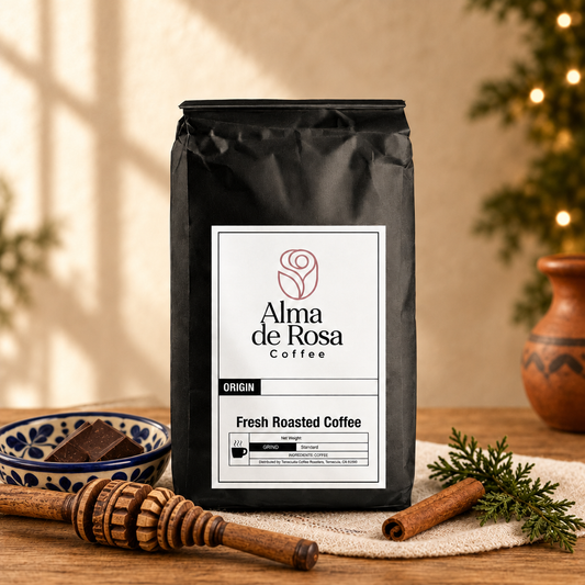 Alma de Rosa Mexican Chocolate Blend coffee bag styled with a wooden molinillo, Talavera-style dish, chocolate and cinnamon